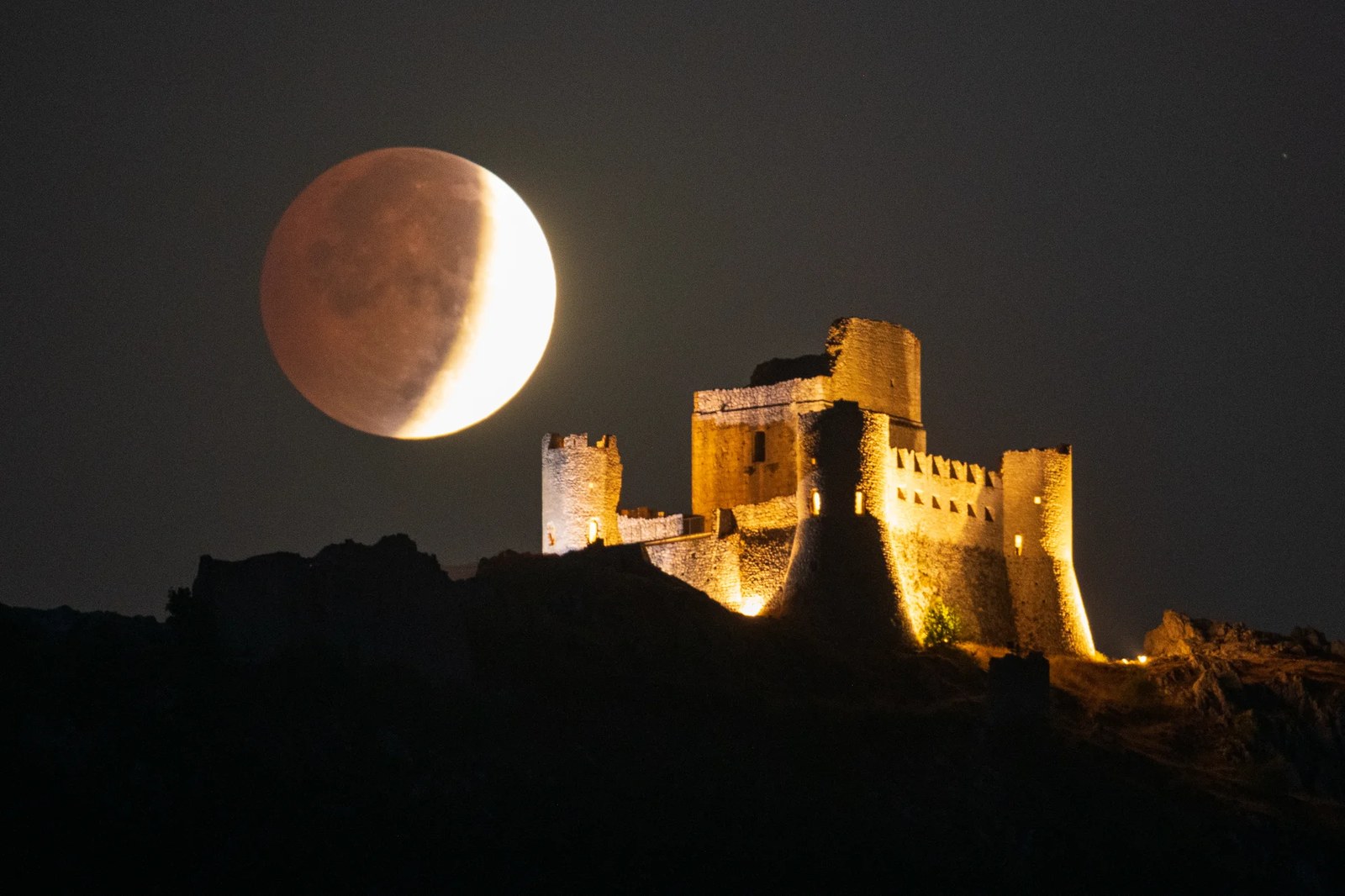 The moon looms large above a fortress.