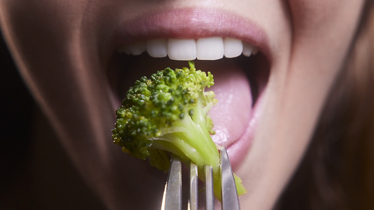 Young woman mouth eating broccoli