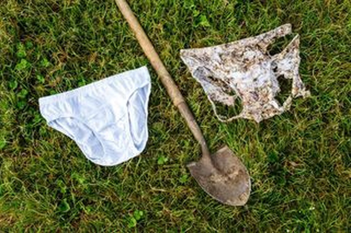 A clean white pair of cotton underwear next to a garden shovel and a badly decomposed, soil-stained pair after two months buried underground