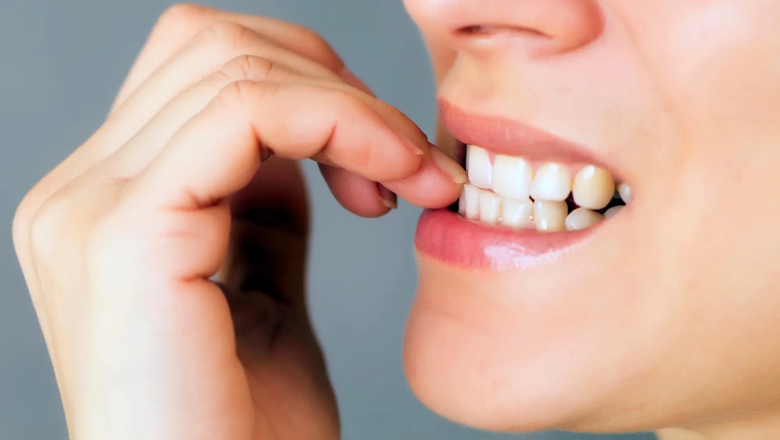 nervous young woman biting her nails on gray background