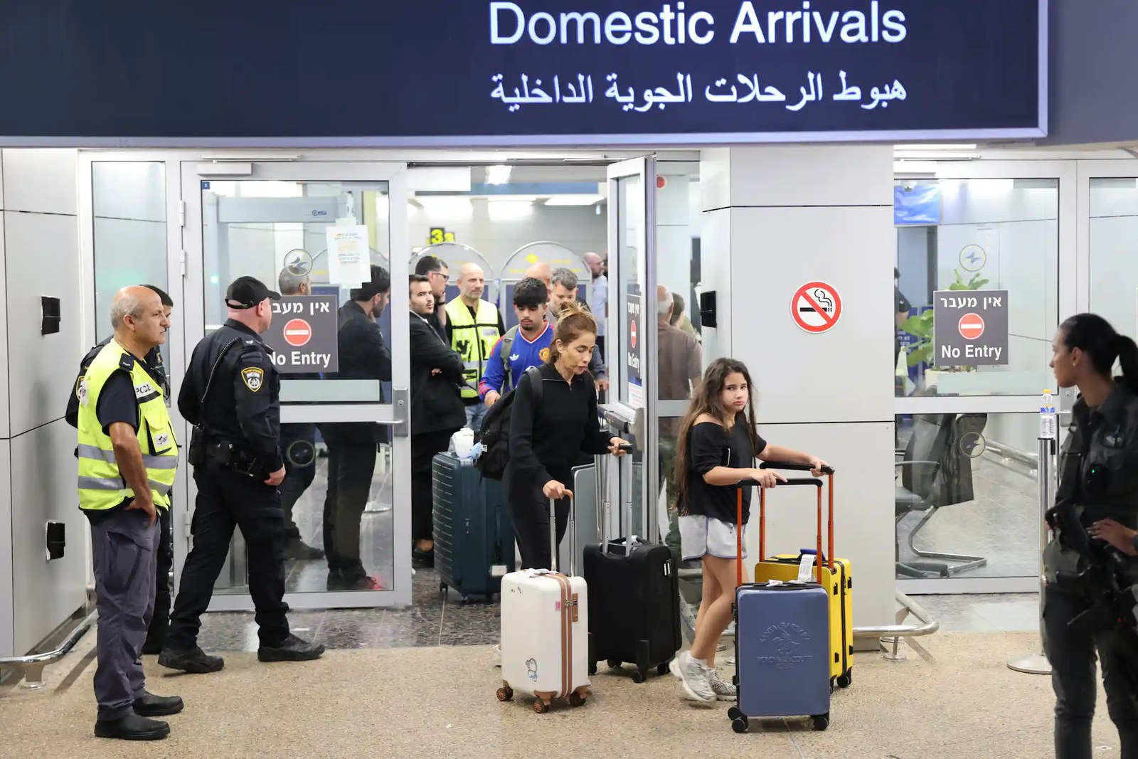 Passengers pushing luggage walk under a sign that says 'Domestic Arrivals'