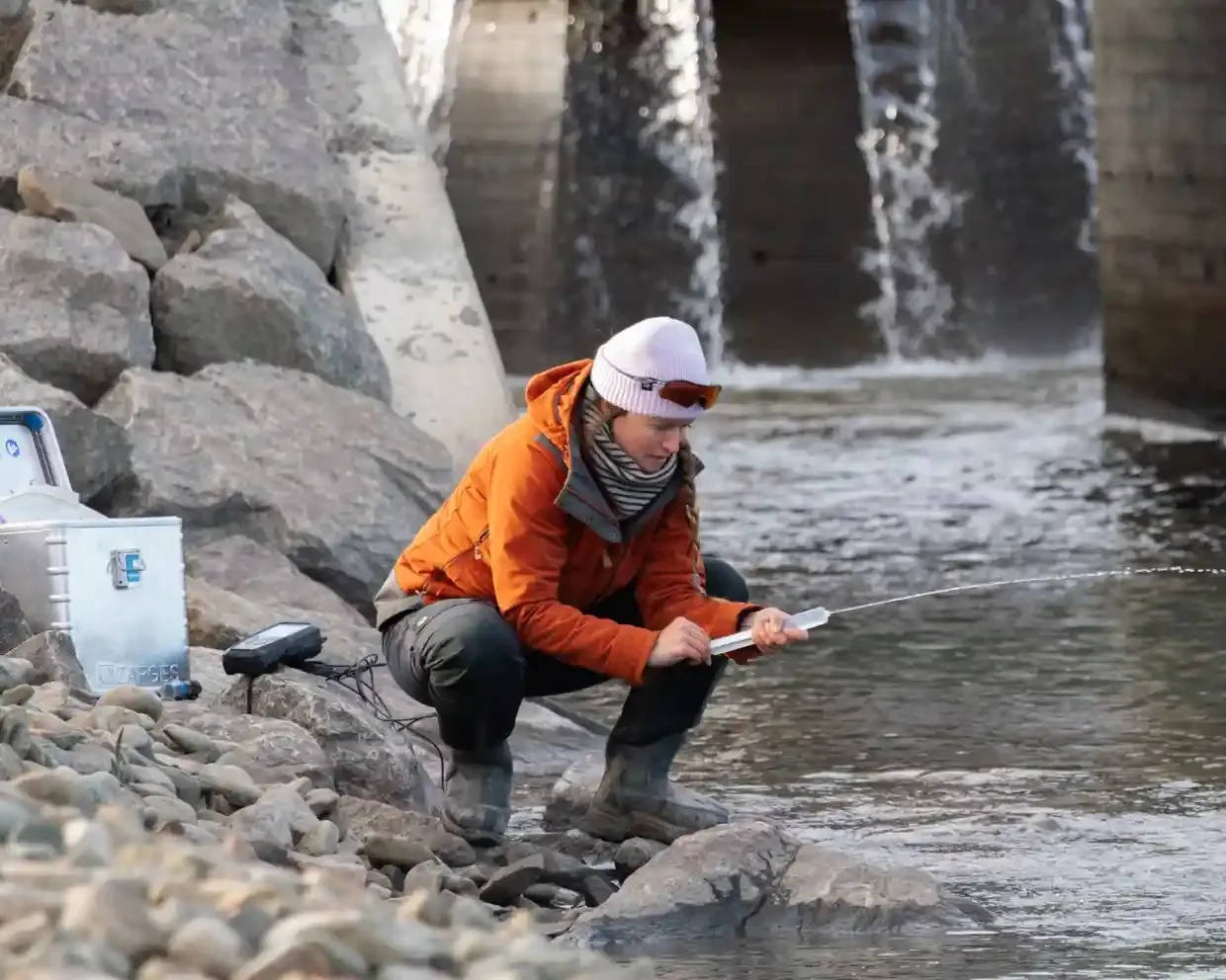 A woman crouches by a body of water squirting water from a syringe
