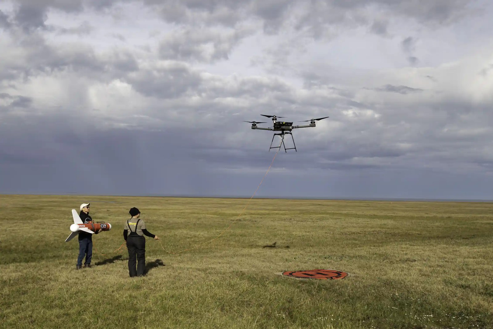 Two scientists operate a drone over a marshy area.