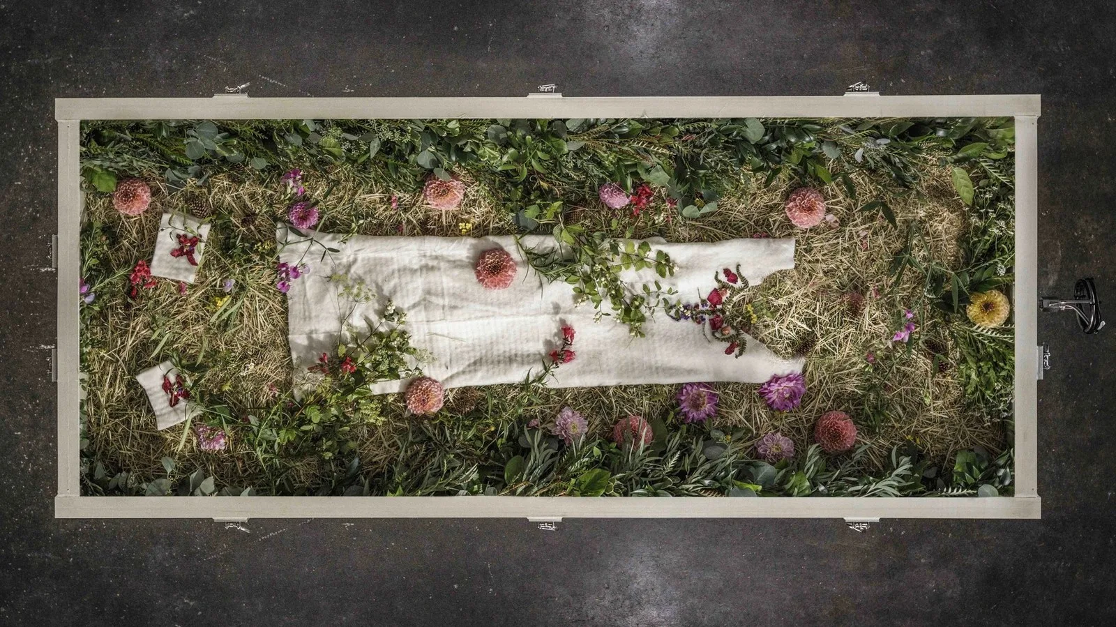 human composting vessel filled with straw and decorated with flowers and white shift.