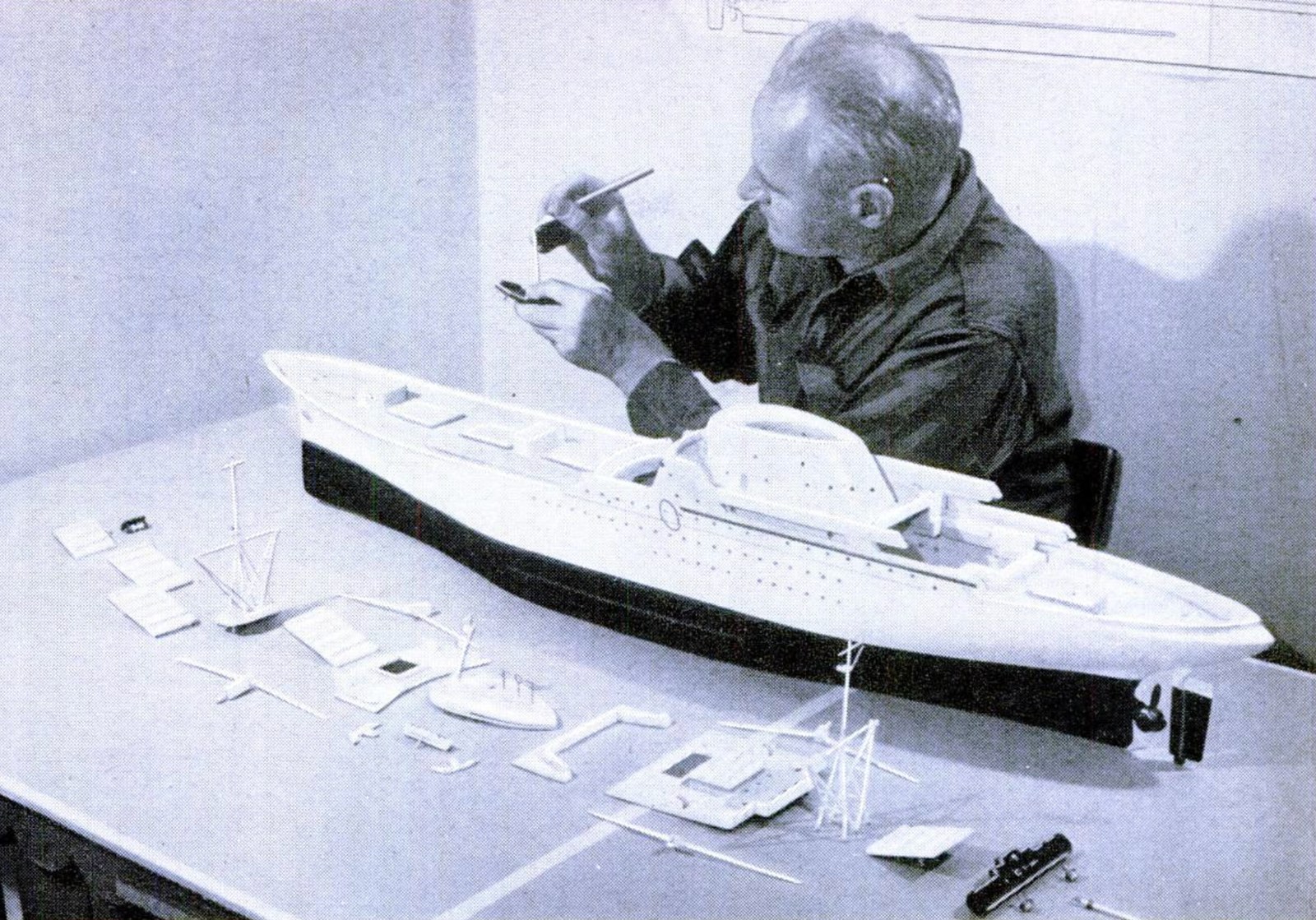 Black and white image of a white man assembling a ship model.